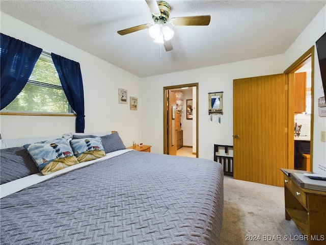 bedroom with a textured ceiling, light colored carpet, ensuite bath, and ceiling fan