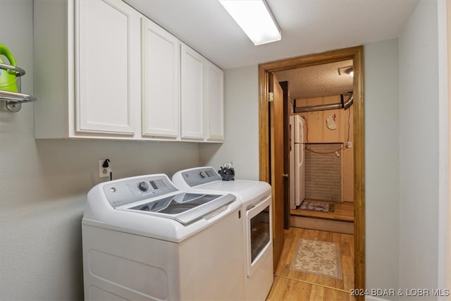 laundry area with cabinets, light hardwood / wood-style flooring, a textured ceiling, and washer and clothes dryer