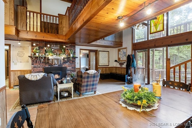 living room with wood ceiling, light wood-type flooring, beamed ceiling, a towering ceiling, and wooden walls