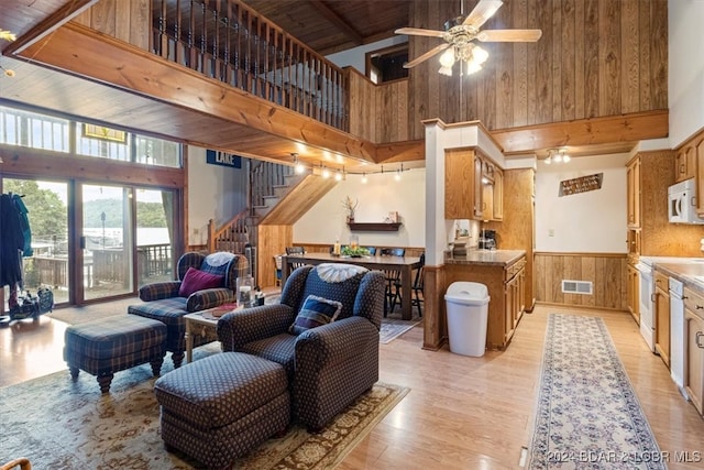 living room with wood ceiling, light wood-type flooring, a towering ceiling, and wood walls