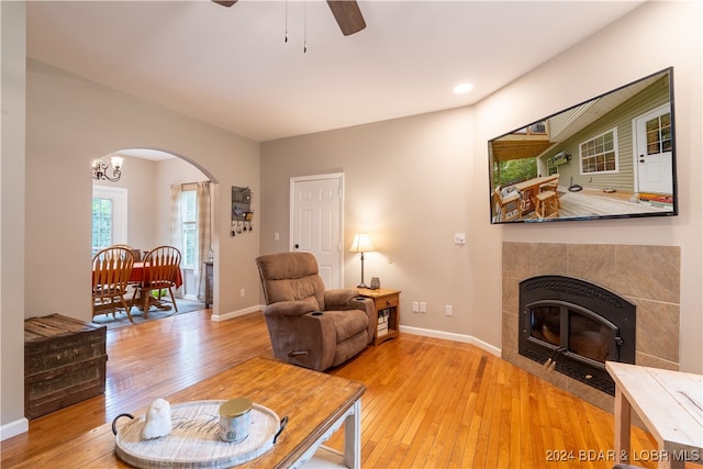 living room with light wood-type flooring, a tiled fireplace, and ceiling fan