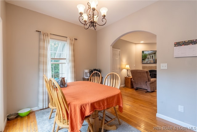 dining space with light wood-type flooring, a tiled fireplace, and a chandelier