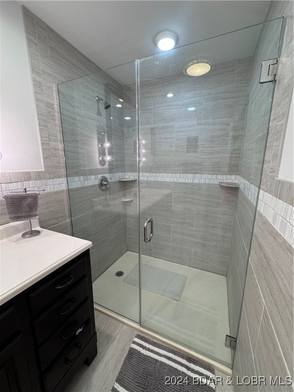 bathroom with hardwood / wood-style floors, tile walls, vanity, and walk in shower