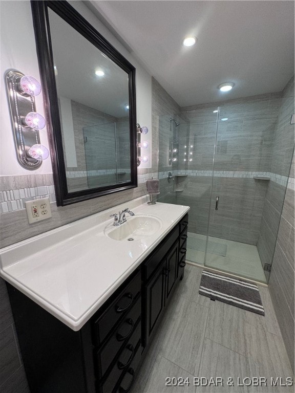 bathroom with a shower with door, vanity, and tile walls