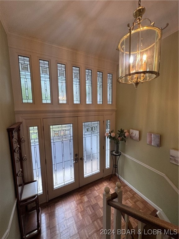 foyer entrance with french doors, ornamental molding, parquet floors, and a notable chandelier