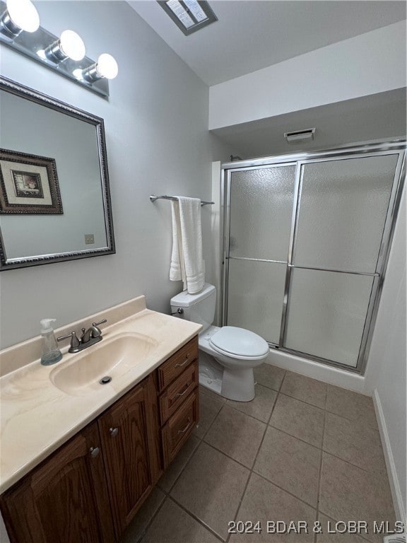 bathroom with vanity, a shower with shower door, toilet, and tile patterned floors