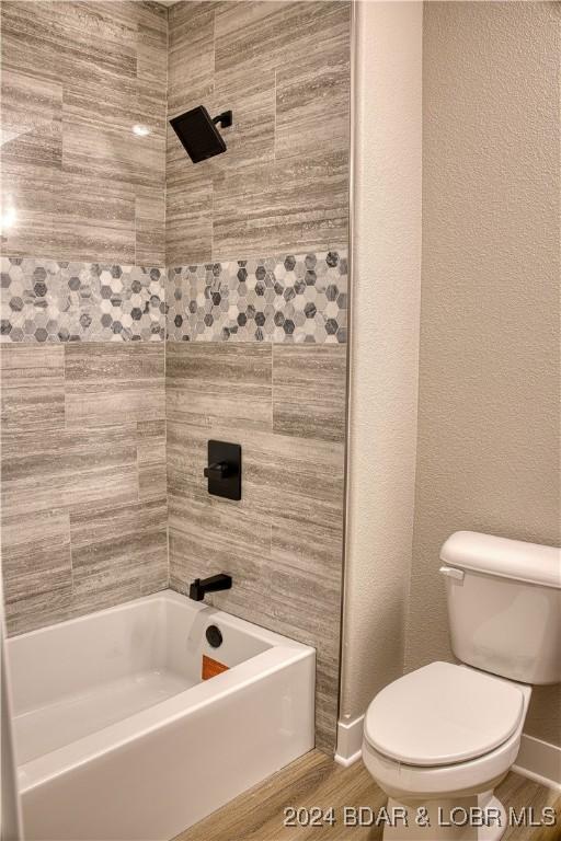 bathroom featuring tiled shower / bath combo, wood-type flooring, and toilet