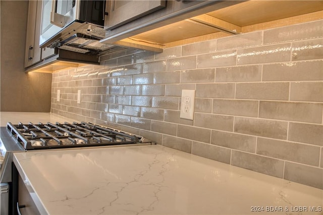 kitchen featuring light stone counters, gas stove, and backsplash