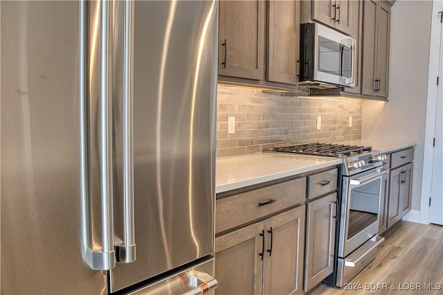 kitchen featuring light stone counters, light wood-type flooring, tasteful backsplash, and appliances with stainless steel finishes