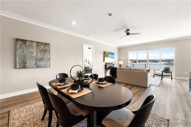 dining space featuring baseboards, ornamental molding, a ceiling fan, and light wood finished floors