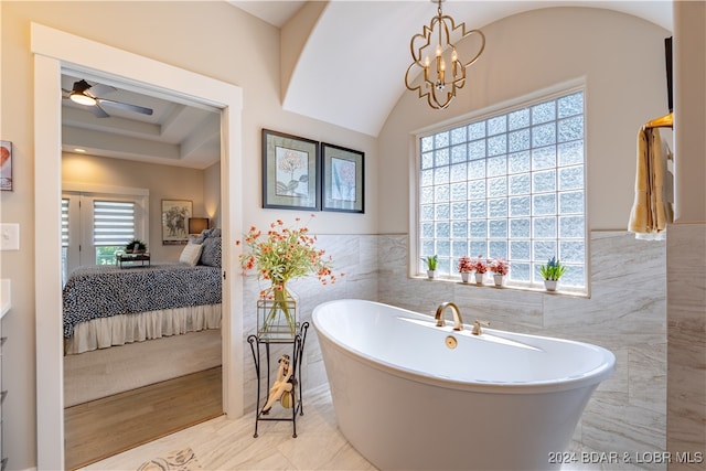 bathroom featuring a tub to relax in, ceiling fan with notable chandelier, hardwood / wood-style floors, a tray ceiling, and tile walls