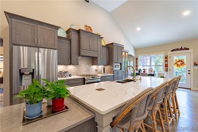 kitchen featuring light hardwood / wood-style flooring, sink, light stone countertops, appliances with stainless steel finishes, and a center island with sink