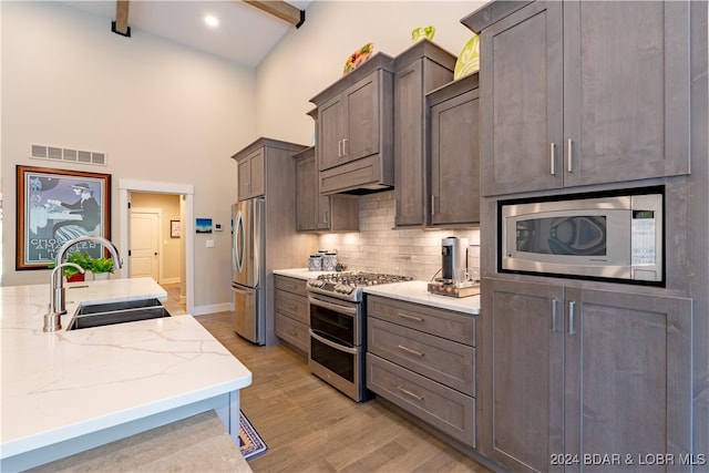 kitchen featuring light stone counters, sink, appliances with stainless steel finishes, and beam ceiling