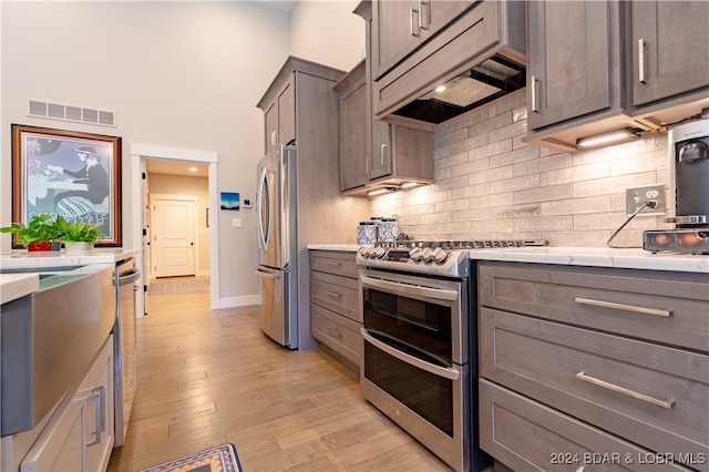 kitchen featuring custom range hood, light wood-type flooring, appliances with stainless steel finishes, decorative backsplash, and a towering ceiling