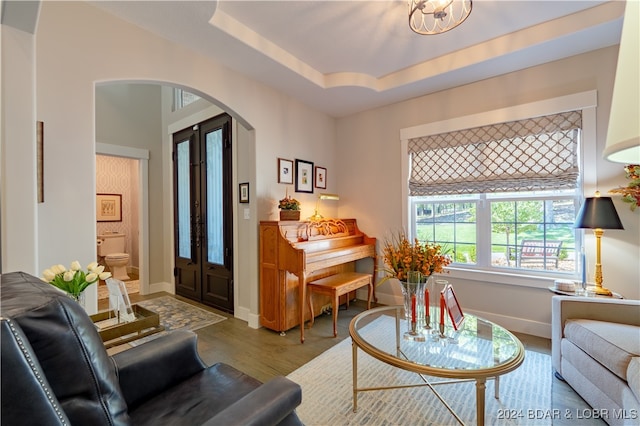 living room featuring an inviting chandelier, light wood-type flooring, and a tray ceiling