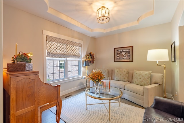 living room featuring hardwood / wood-style flooring, a raised ceiling, and an inviting chandelier