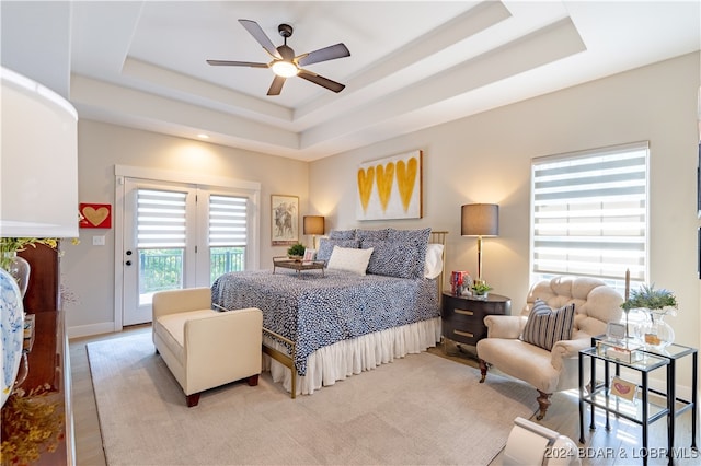 bedroom featuring a raised ceiling, light hardwood / wood-style flooring, access to exterior, and ceiling fan