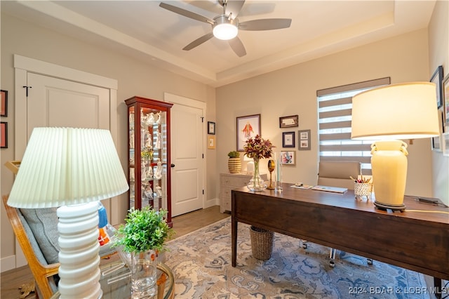 office area with a tray ceiling, hardwood / wood-style flooring, and ceiling fan