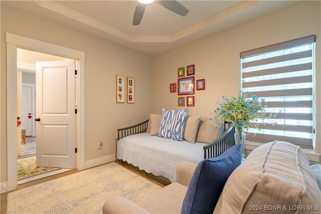 bedroom with light wood-type flooring, ceiling fan, and a raised ceiling