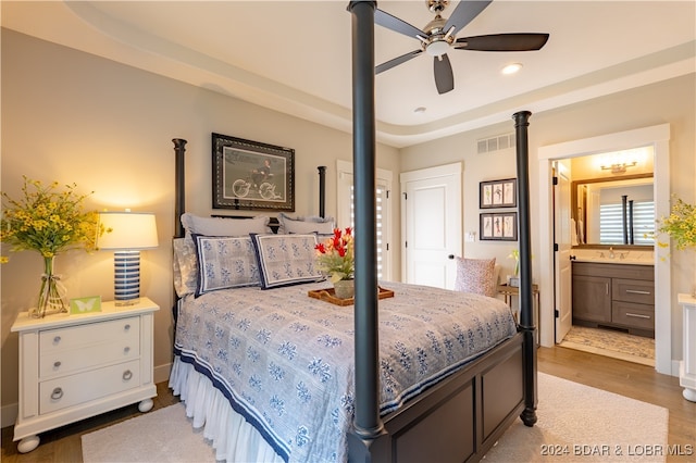 bedroom featuring ensuite bath, sink, ceiling fan, a tray ceiling, and hardwood / wood-style flooring