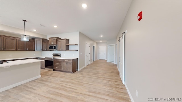 kitchen featuring a barn door, dark brown cabinetry, pendant lighting, appliances with stainless steel finishes, and light hardwood / wood-style floors