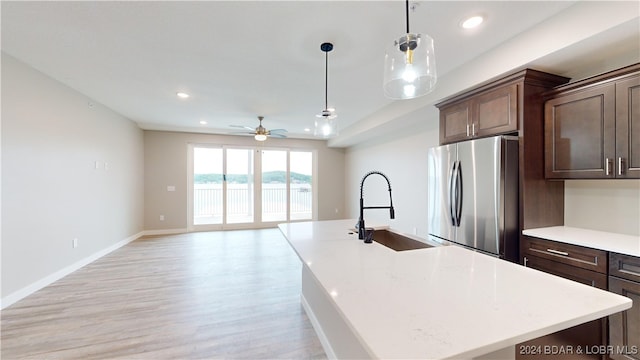 kitchen featuring a kitchen island with sink, light hardwood / wood-style flooring, sink, decorative light fixtures, and stainless steel refrigerator