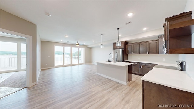 kitchen with hanging light fixtures, light hardwood / wood-style floors, stove, stainless steel refrigerator, and a kitchen island with sink