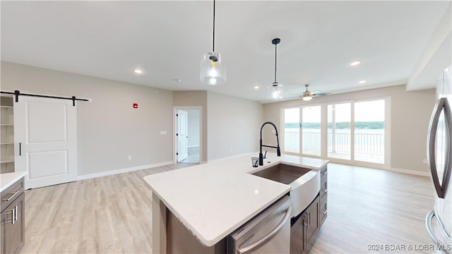 kitchen featuring a kitchen island with sink, a barn door, light wood-type flooring, pendant lighting, and stainless steel appliances