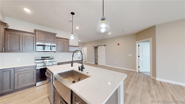 kitchen with sink, a barn door, light hardwood / wood-style floors, stainless steel appliances, and a center island with sink