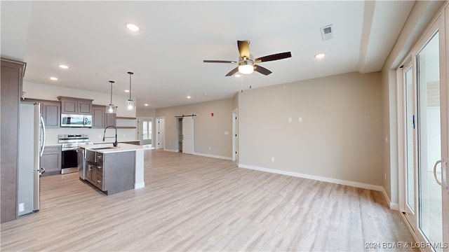 kitchen featuring appliances with stainless steel finishes, a kitchen island with sink, a barn door, light wood-type flooring, and pendant lighting