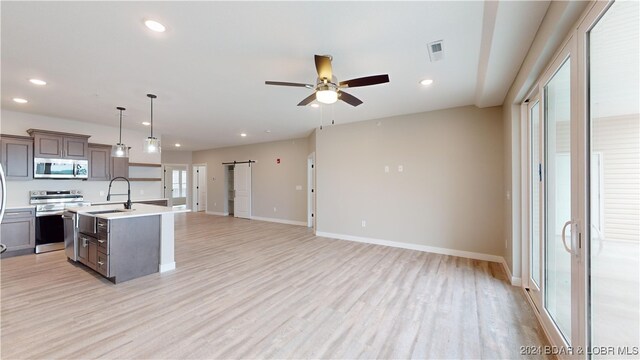 kitchen featuring hanging light fixtures, a kitchen island with sink, a barn door, sink, and stainless steel appliances