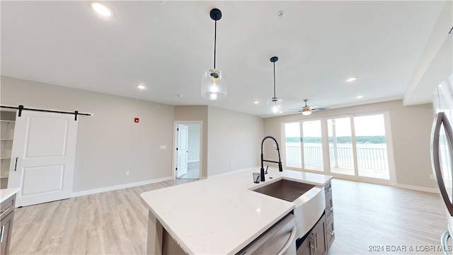 kitchen with hanging light fixtures, ceiling fan, an island with sink, a barn door, and light hardwood / wood-style flooring