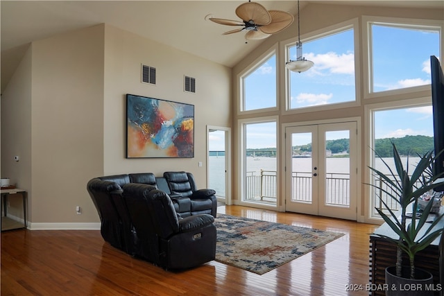 living room featuring high vaulted ceiling, a water view, wood-type flooring, ceiling fan, and french doors