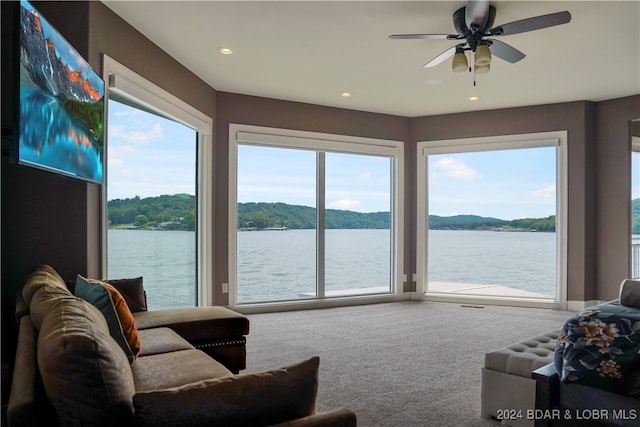 carpeted living room with ceiling fan and a water view