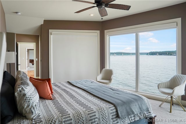 carpeted bedroom with a water view and ceiling fan