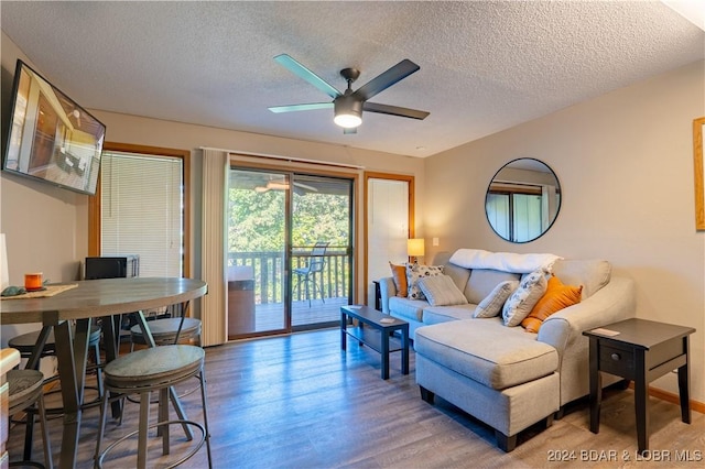 living room featuring ceiling fan, a textured ceiling, baseboards, and wood finished floors