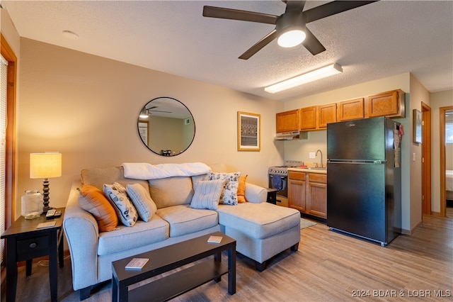 living room featuring light wood-type flooring, ceiling fan, and a textured ceiling