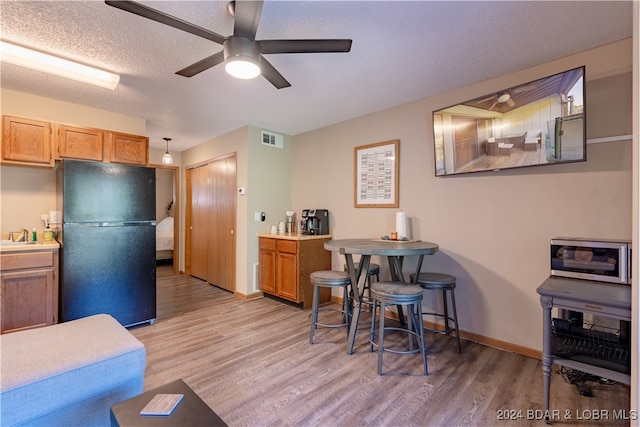 kitchen featuring baseboards, visible vents, freestanding refrigerator, a textured ceiling, and light wood-type flooring