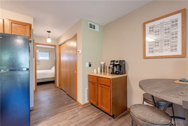 kitchen featuring visible vents, light wood-style flooring, freestanding refrigerator, and brown cabinets