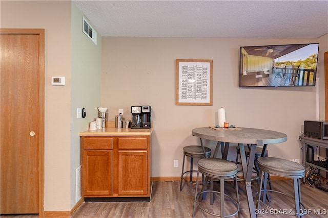 bar with a textured ceiling, light wood-type flooring, visible vents, and baseboards