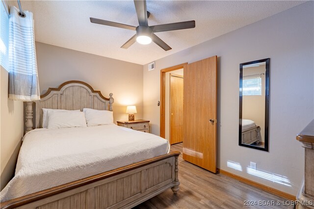 bedroom with a textured ceiling, light wood-style flooring, visible vents, baseboards, and a ceiling fan