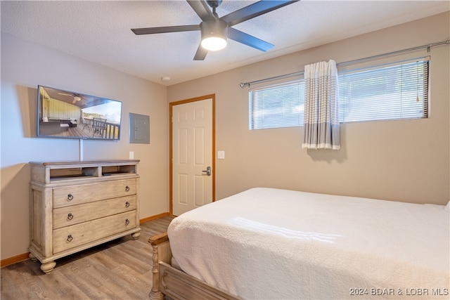 bedroom with electric panel, baseboards, a ceiling fan, wood finished floors, and a textured ceiling