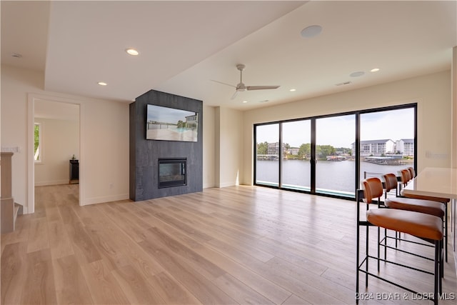 unfurnished living room with light wood-type flooring, a water view, a large fireplace, and ceiling fan