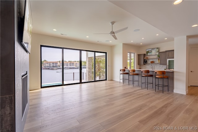 kitchen featuring sink, a kitchen bar, light hardwood / wood-style flooring, a water view, and ceiling fan