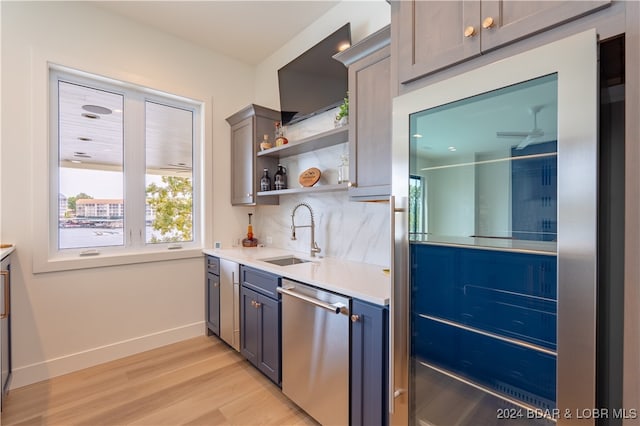 kitchen with sink, stainless steel dishwasher, light hardwood / wood-style flooring, backsplash, and gray cabinets