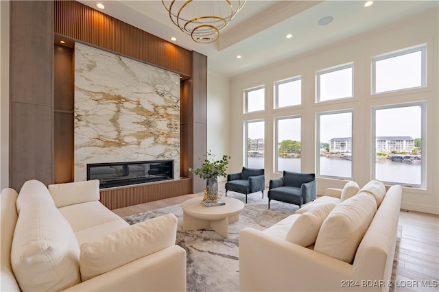 living room featuring light hardwood / wood-style floors, a water view, a towering ceiling, an inviting chandelier, and a premium fireplace