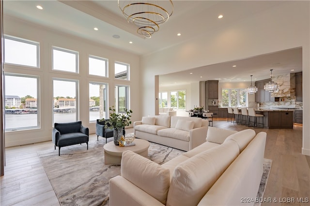 living room with a notable chandelier, a towering ceiling, and light hardwood / wood-style flooring