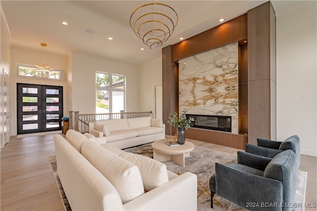 living room featuring light wood-type flooring, a chandelier, a premium fireplace, and french doors