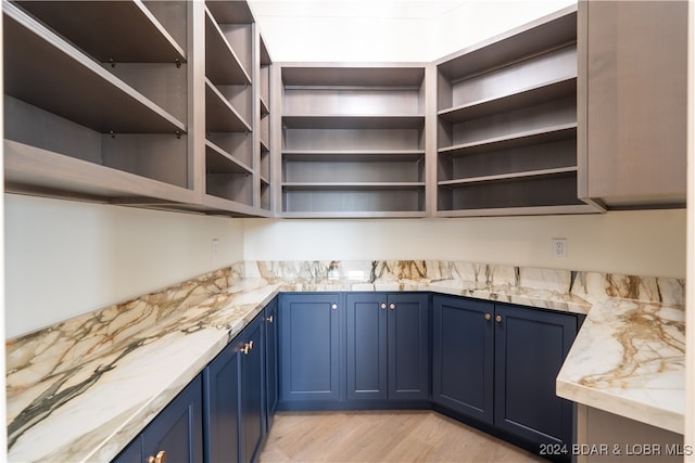 interior space with light hardwood / wood-style floors, blue cabinets, and light stone countertops