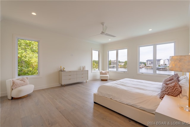 bedroom with ceiling fan, a water view, light hardwood / wood-style flooring, and multiple windows